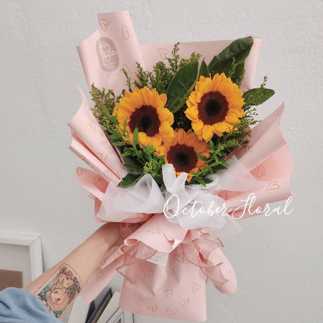 Pink Heart-Patterned Wrapped Bouquet with Three Sunflowers and Green Foliage