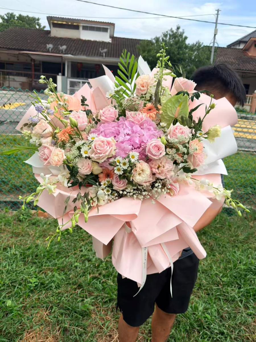 Pink Romance - Mega Hand-Tied Bouquet in Multi-Layer Pink Packaging Featuring a Central Pink Hydrangea, Pink Roses, Small White Daisies, and Green Foliage